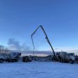 Concrete pumping trucks operating on a snowy construction site in Alaska at sunset