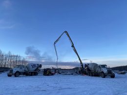 Concrete pumping trucks operating on a snowy construction site in Alaska at sunset