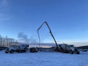 Concrete pumping trucks operating on a snowy construction site in Alaska at sunset