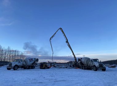 Concrete pumping trucks operating on a snowy construction site in Alaska at sunset