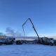 Concrete pumping trucks operating on a snowy construction site in Alaska at sunset