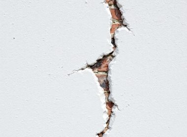Close-up of a large crack in a white concrete wall exposing red bricks underneath