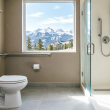 Modern accessible bathroom with stainless steel grab bars near toilet and walk-in shower, featuring scenic Colorado Rocky Mountain view through window, professional home safety modification for seniors aging in place