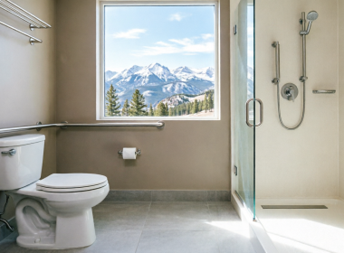 Modern accessible bathroom with stainless steel grab bars near toilet and walk-in shower, featuring scenic Colorado Rocky Mountain view through window, professional home safety modification for seniors aging in place