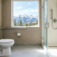 Modern accessible bathroom with stainless steel grab bars near toilet and walk-in shower, featuring scenic Colorado Rocky Mountain view through window, professional home safety modification for seniors aging in place